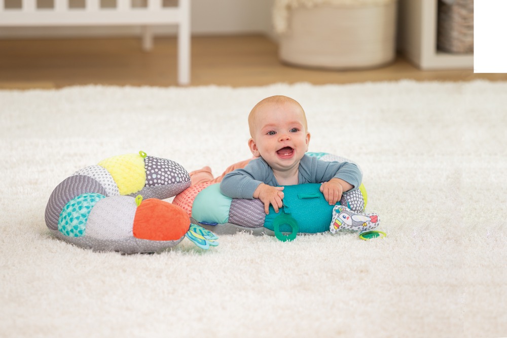 Young baby sat on the floor supported by a colourful pillow