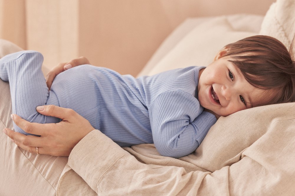 A baby wearing a blue MORI sleepsuit lying on someone's chest