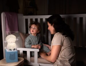 Child in a cot beside a woman with a Sleepy Sheep Tonie Night Light on the bedside table