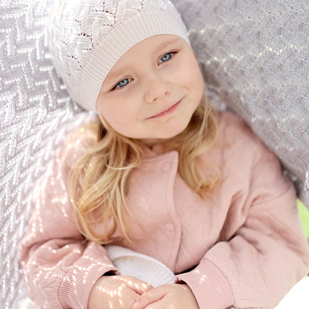 Young girl wearing a knitted hat sat beneath a knitted blanket 