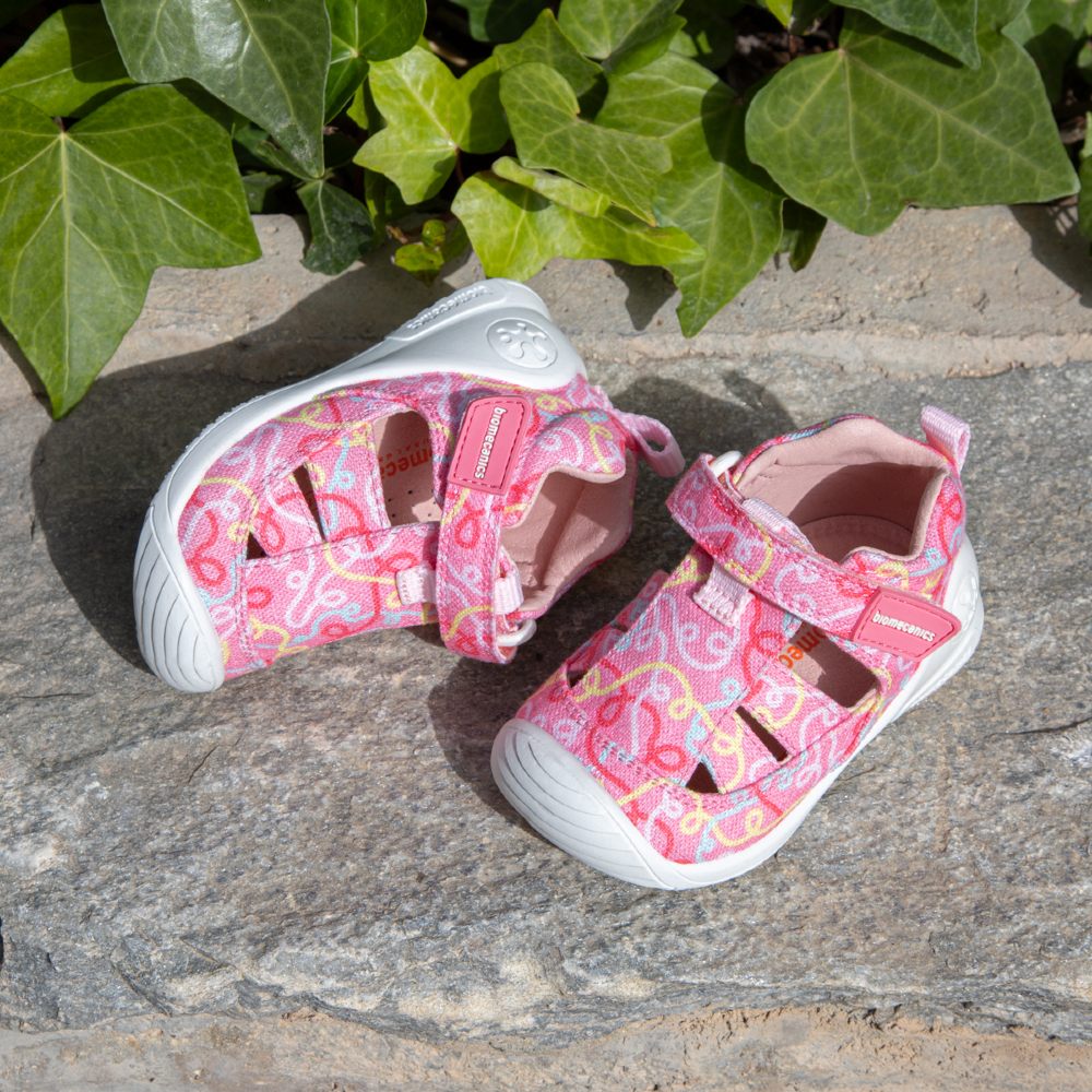 A pink pair of children's shoes displayed outside on a stone floor 
