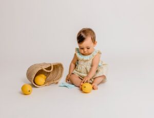 Baby sat on the floor playing with a backet of lemons