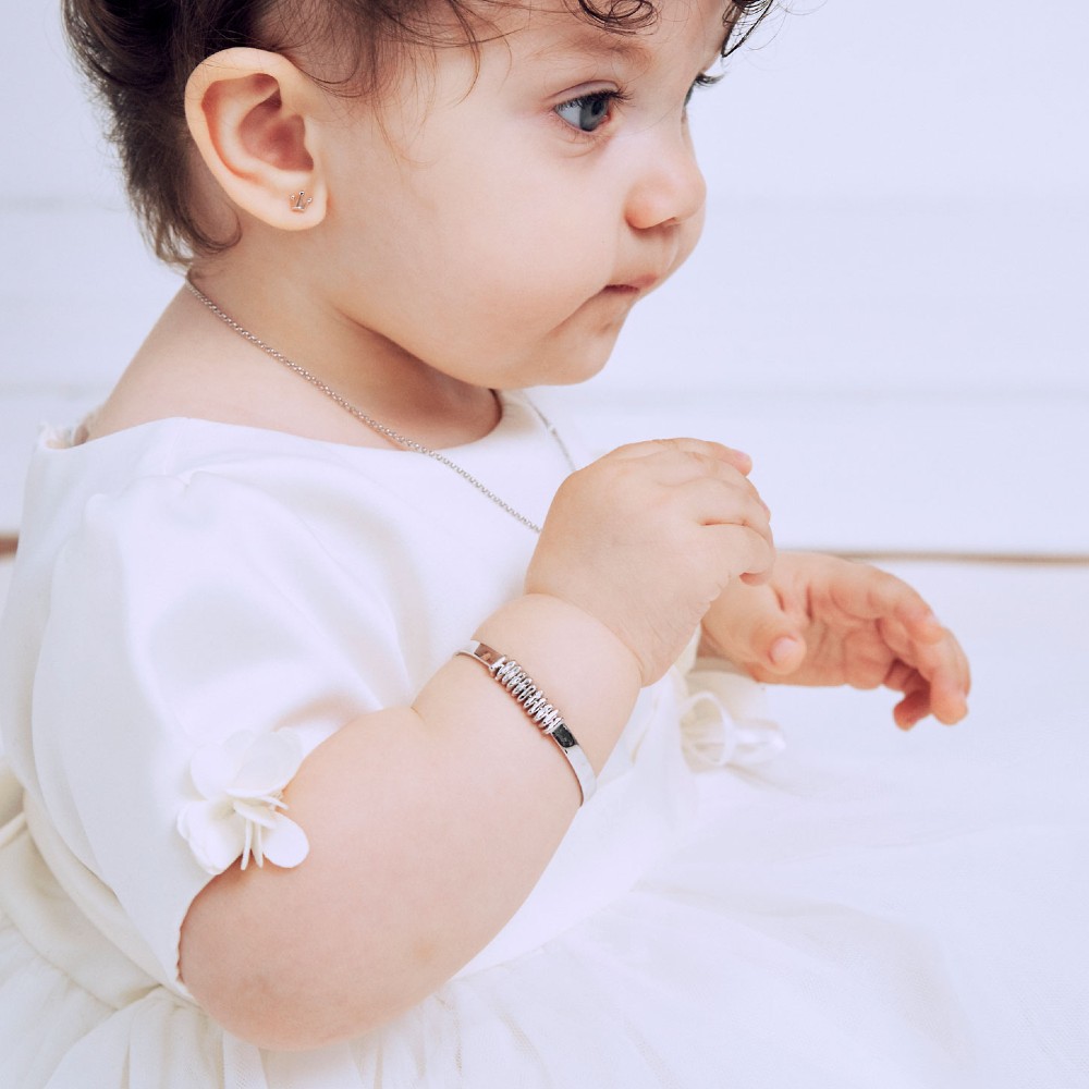 Young baby in a white dress wearing a silver bracelet 