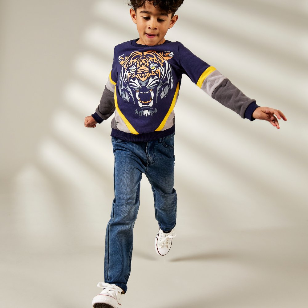 Boy running towards the camera wearing a top with a lion's head on and jeans 