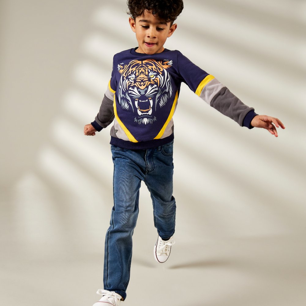 Young boy running towards the camera wearing a sweatshirt with a lion's head on the front with jeans