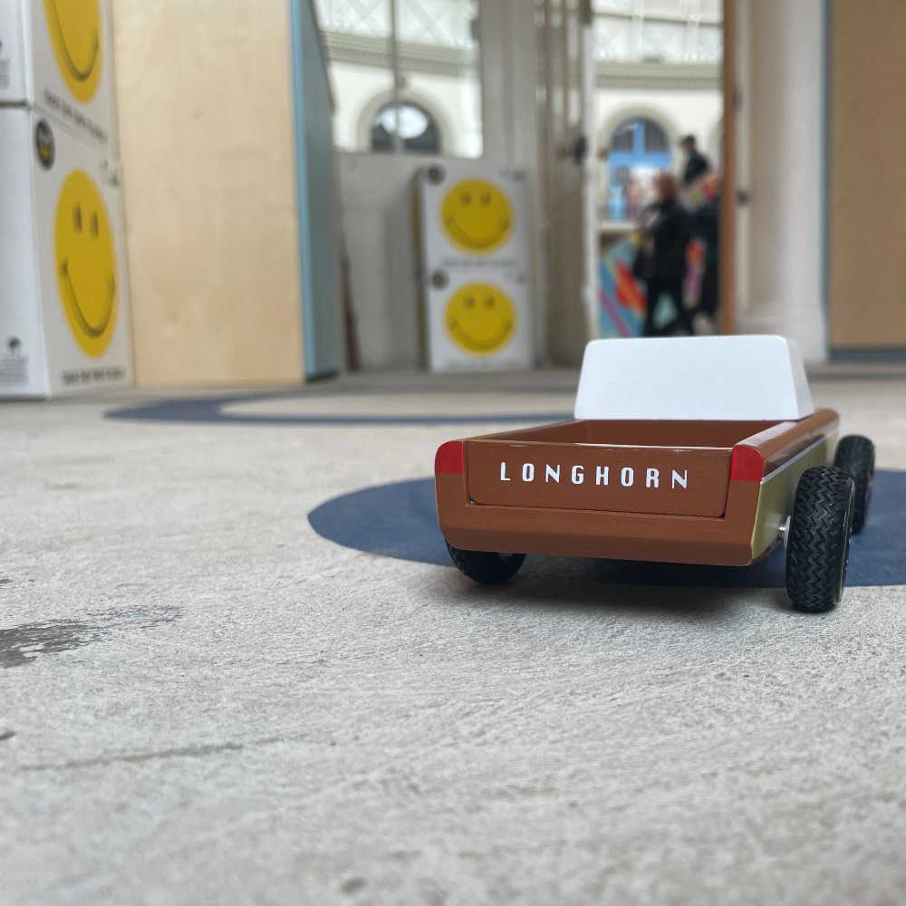 A wooden toy car on the floor of a shop