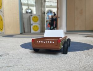 A wooden toy car on the floor of a shop