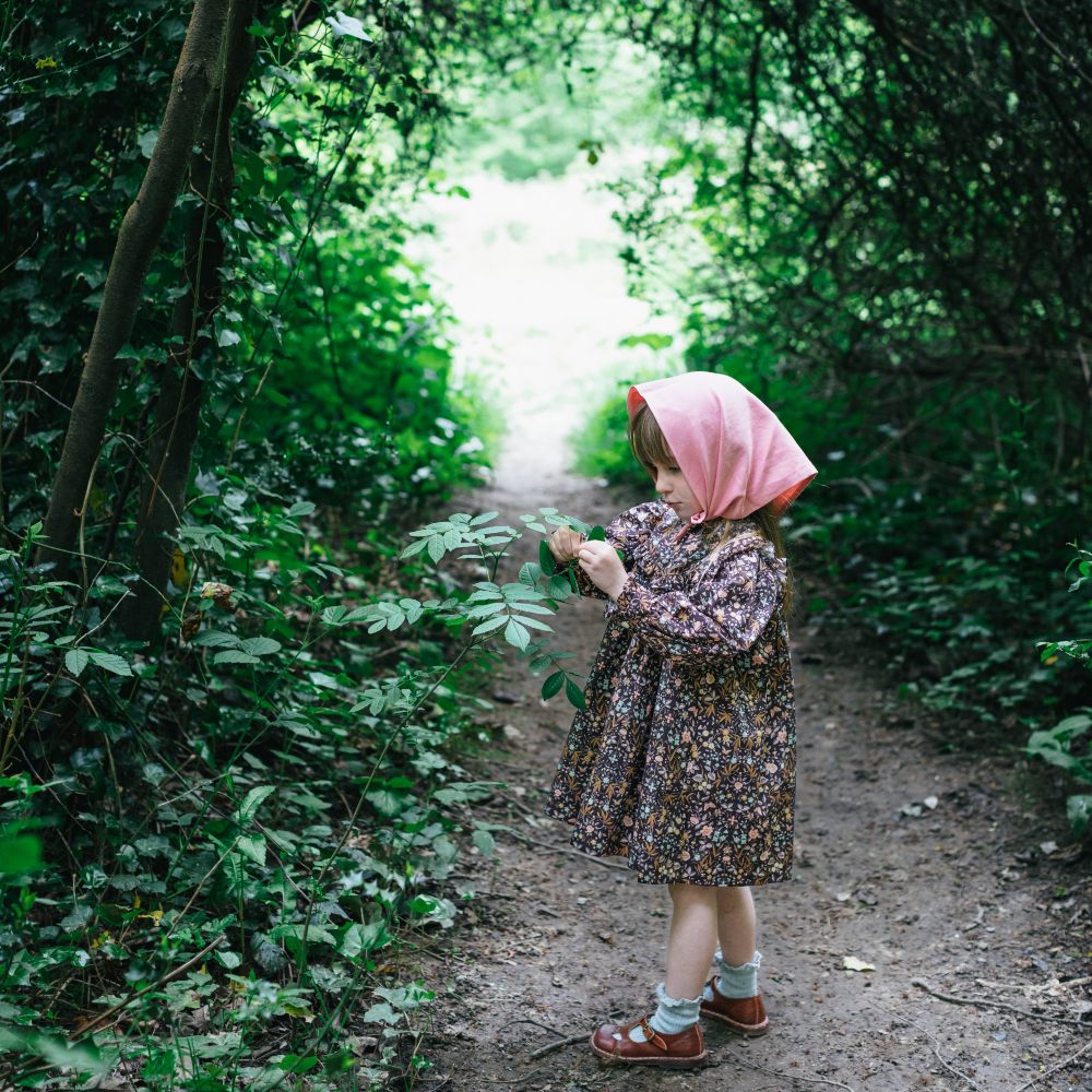 Girl wearing a headscarf and dress stood on a path in a wood
