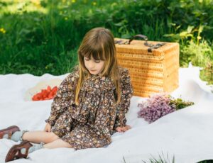 Girl sat outside on a picnic blanket wearing a dress by Ira & Isla