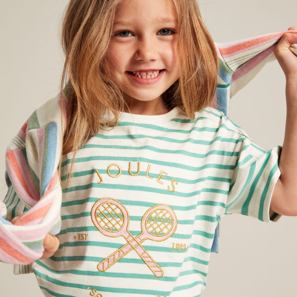 Young girl smiling wearing a green striped top with the Joules logo on the front 
