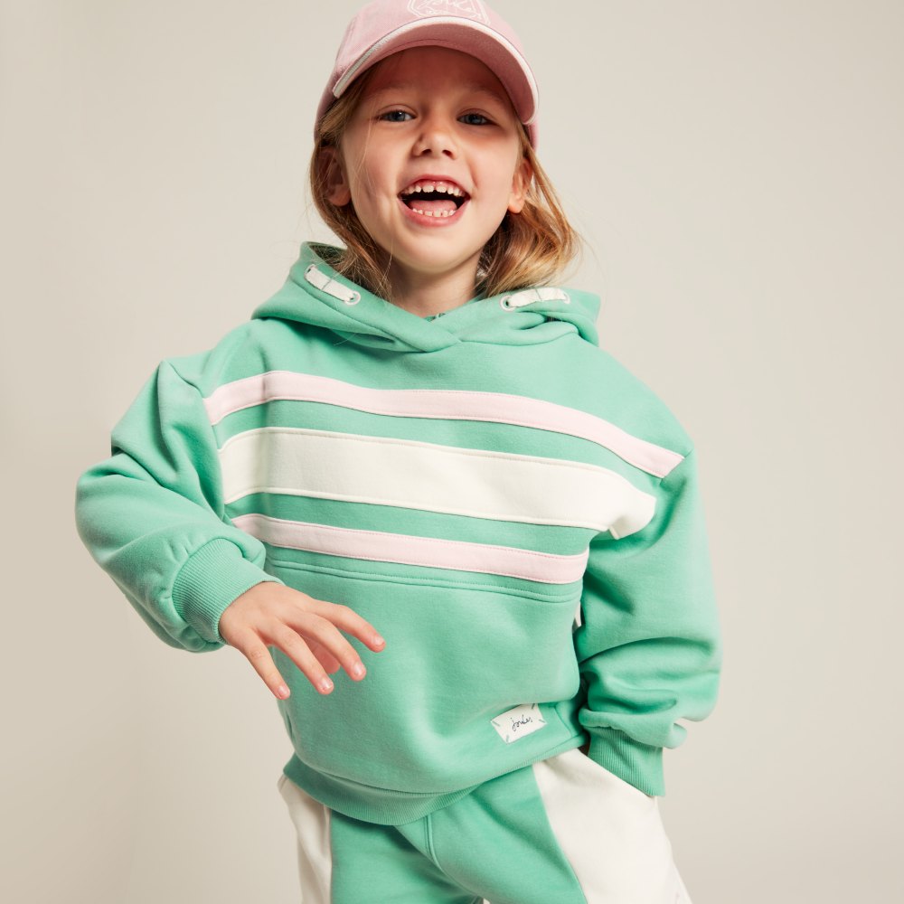 Young girl in a pink cap wearing a green and white hoody and shorts from the Joules s/s24 childrenswear collection 