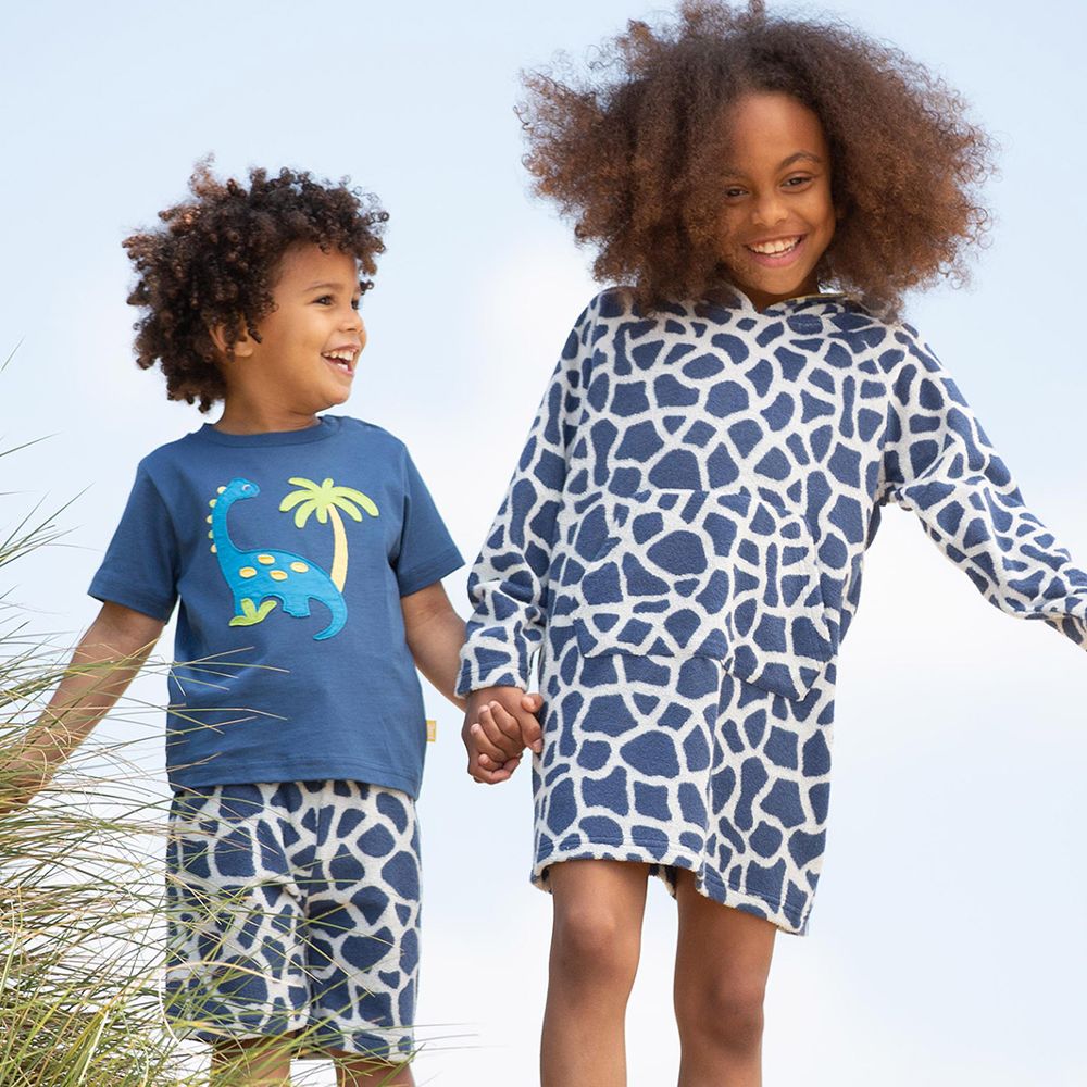 Two young children holding hands on a beach wearing blue giraffe print clothing 