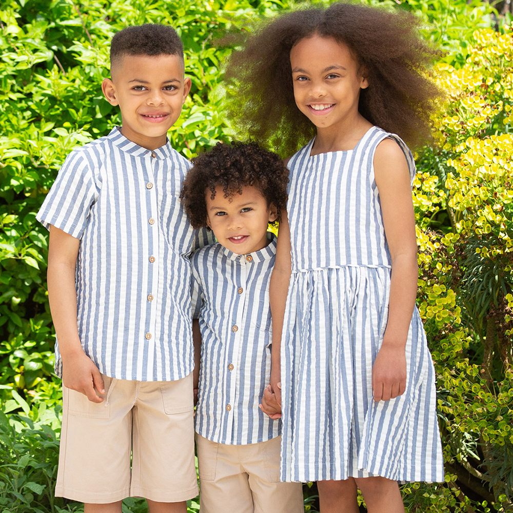 Three children stood together wearing matching blue and white stripe outfits by Kite Clothing 