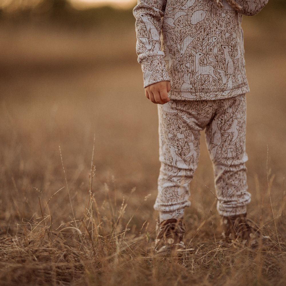 A young child stood in a field with their body and legs showing wearing a printed top and trousers 