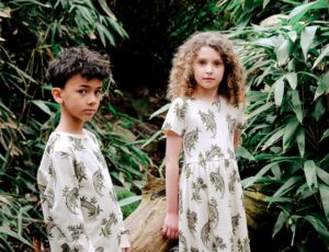 Two children stood in a wood wearing outfits with animal prints on them by MAI