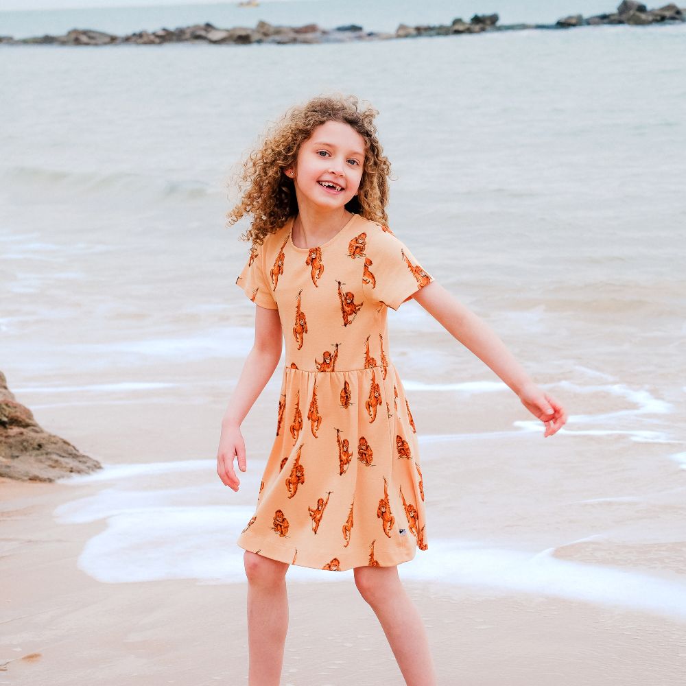 Girl stood on a beach by the sea wearing an orange dress with a monkey print 