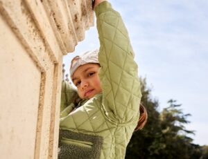 Young girl hanging off a wall wearing a pale green jacket