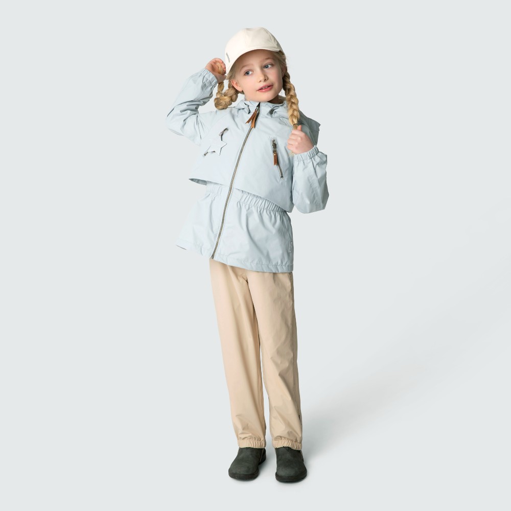 A young girl wearing a hat, blue outerwear jacket and beige trousers 