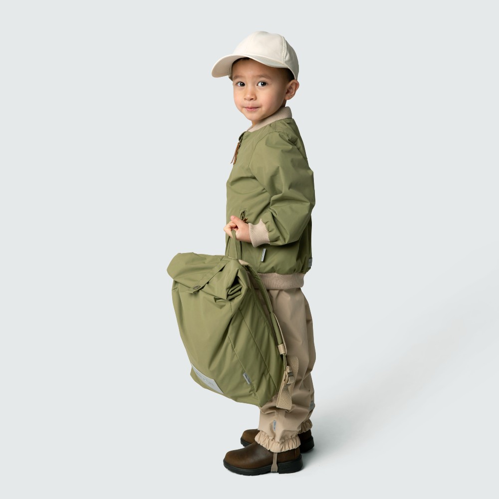 Young boy stood side on wearing a hat, jacket and trousers and holding a bag