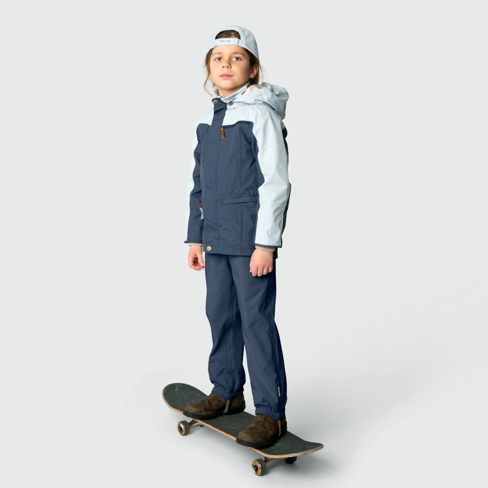 Young child stood on a skate board in a blue outerwear jacket and trousers 