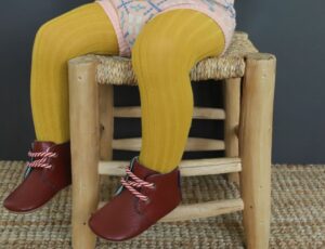 Image of a child's legs sat on a chair wearing yellow tights and dark red shoes