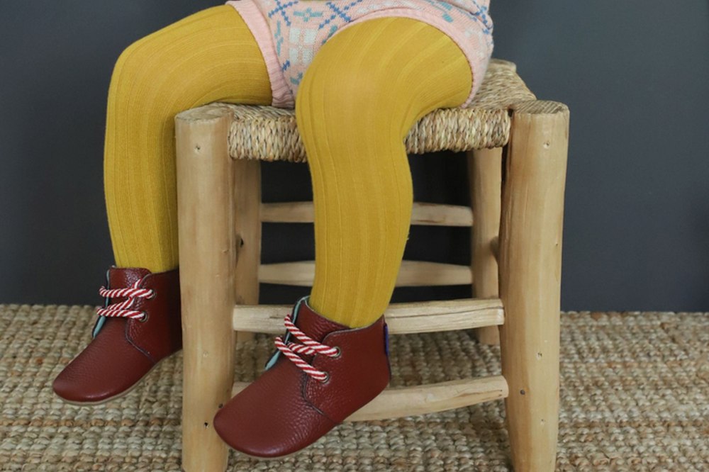 Image of a child's legs sat on a chair wearing yellow tights and dark red shoes