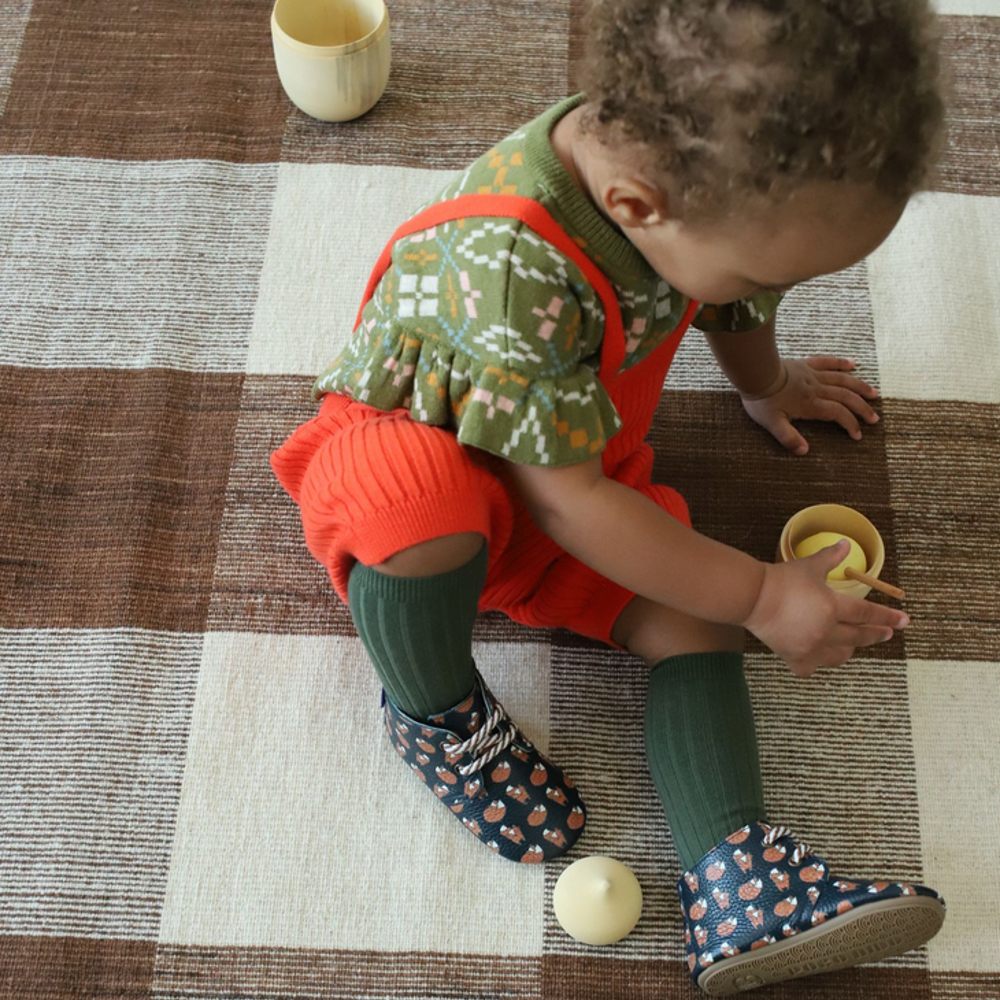 Young child sat on a brown and white checked rug playing with a toy 