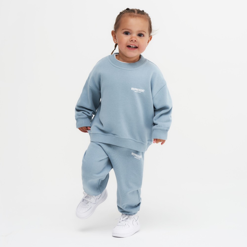Young child wearing a pale blue sweatshirt and sweatpants from the Mini Owners' Club Collection by Represent 