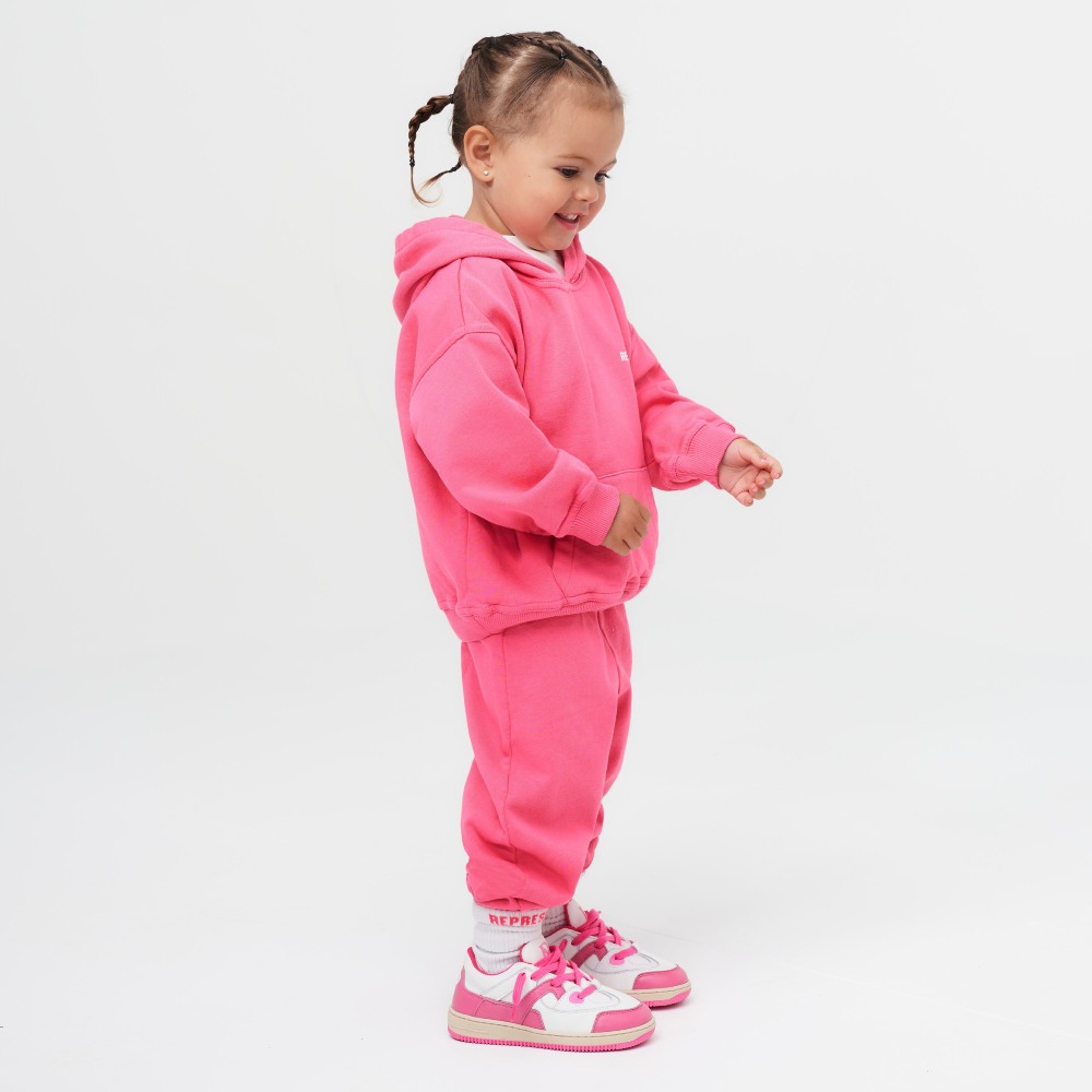 Young girl stood side on wearing a pink hoody and sweatpants from the Mini Owners' Club Collection by Represent
