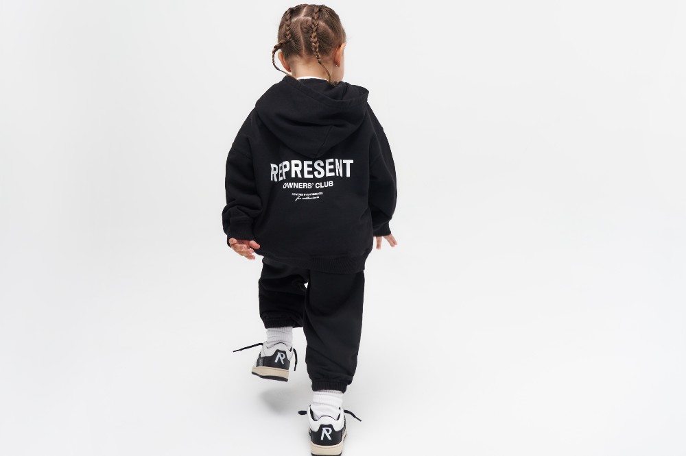 Young child with their back to the camera wearing a black hoodie and sweatpants from the Mini Owners' collection by Represent