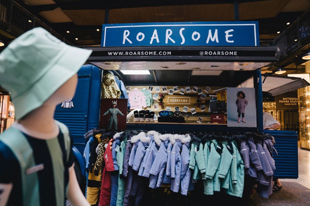 A vintage blue van with Roarsome written on it displaying a range of children's clothes on a rail 