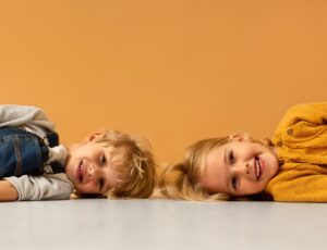 A young boy and girl lying on the floor on their sides smiling at the camera