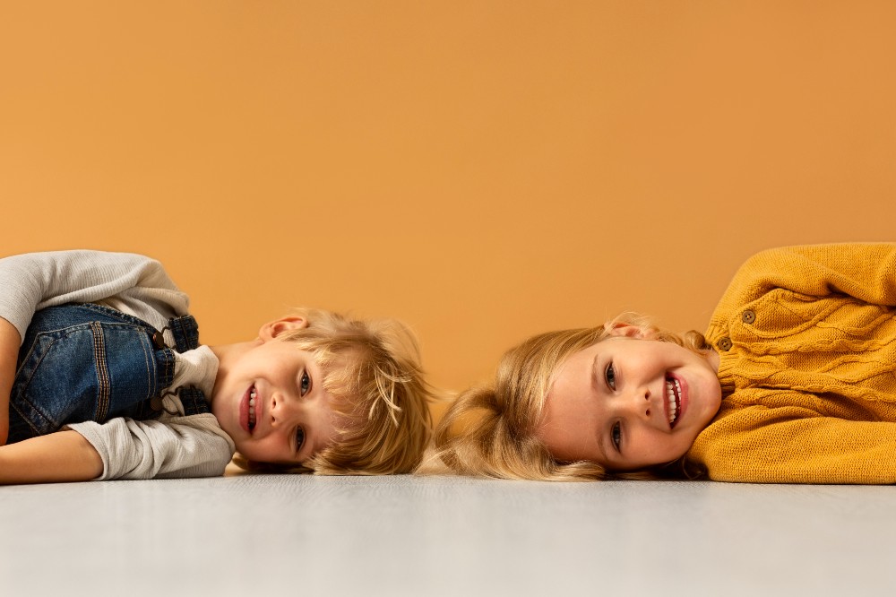 A young boy and girl lying on the floor on their sides smiling at the camera