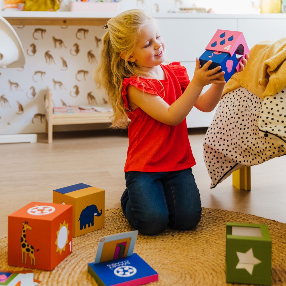 Young girl knelt on the floor playing with brightly coloured cubes with animals on them by SmartGames