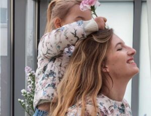 A young girl holding a pink flower up to a woman's head