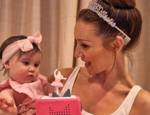 A woman wearing a tiara holding a young baby looking at a pink Angelina Ballerina Toniebox