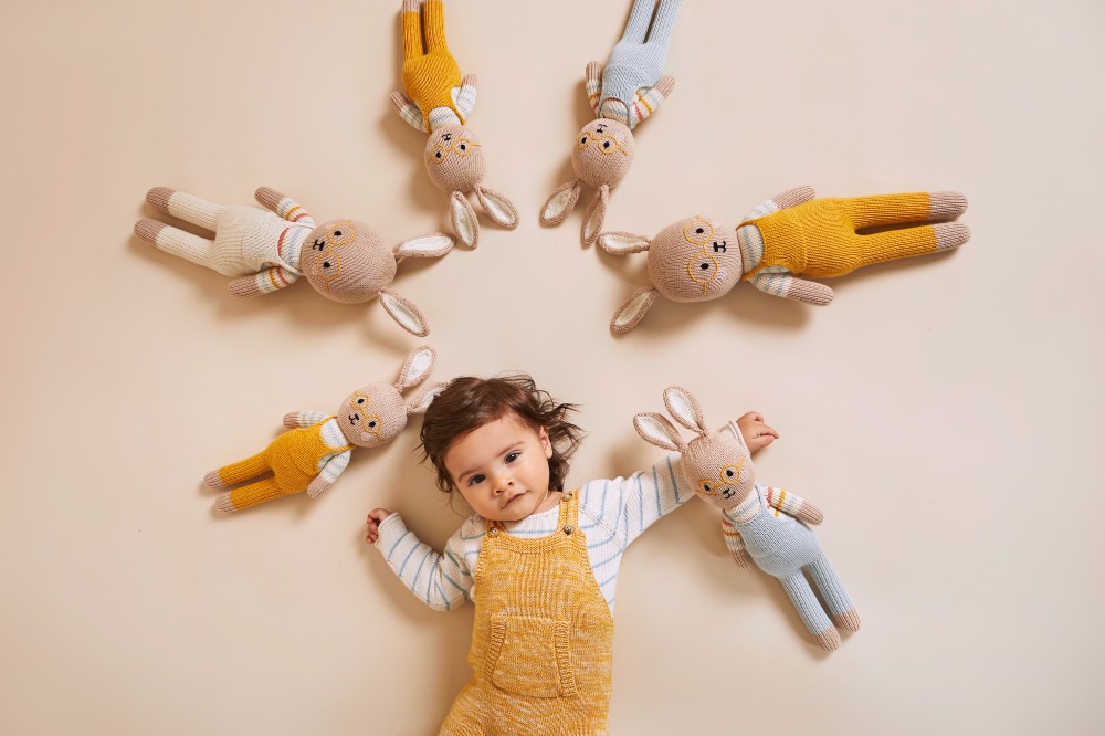 Young child lying on the floor surrounded by knitted toy rabbits