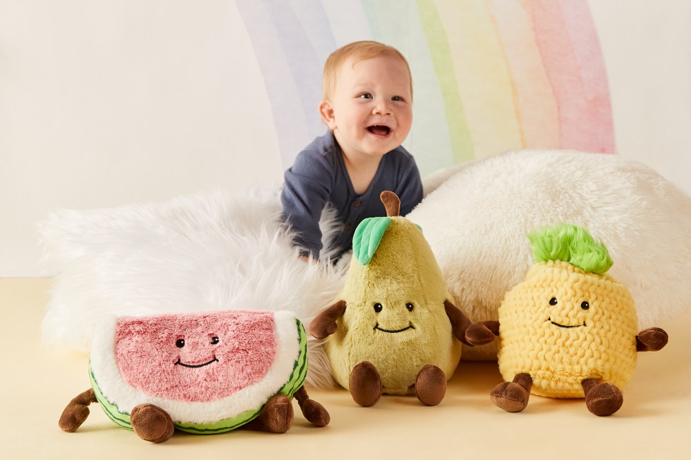 Baby sat in front on a rainblow background surrounded by fruit shaped soft toys
