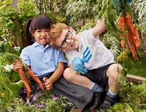 Two young children sat in the garden holding up carrots