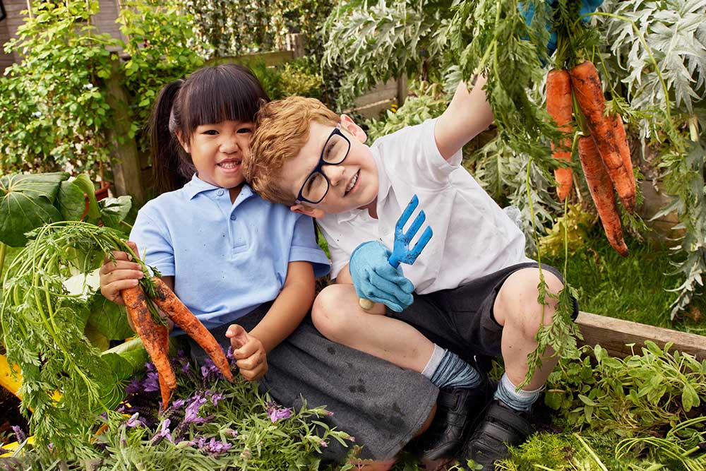 Two young children sat in the garden holding up carrots