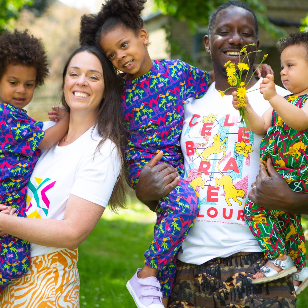 A man and woman stood outside holding young children wearing brightly coloured outfits 