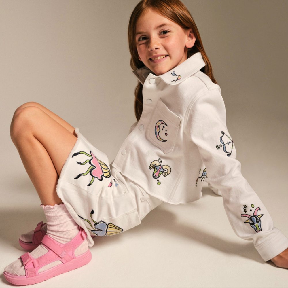A young girl sat on the floor wearing a shirt, shorts and pink sandals with white socks 