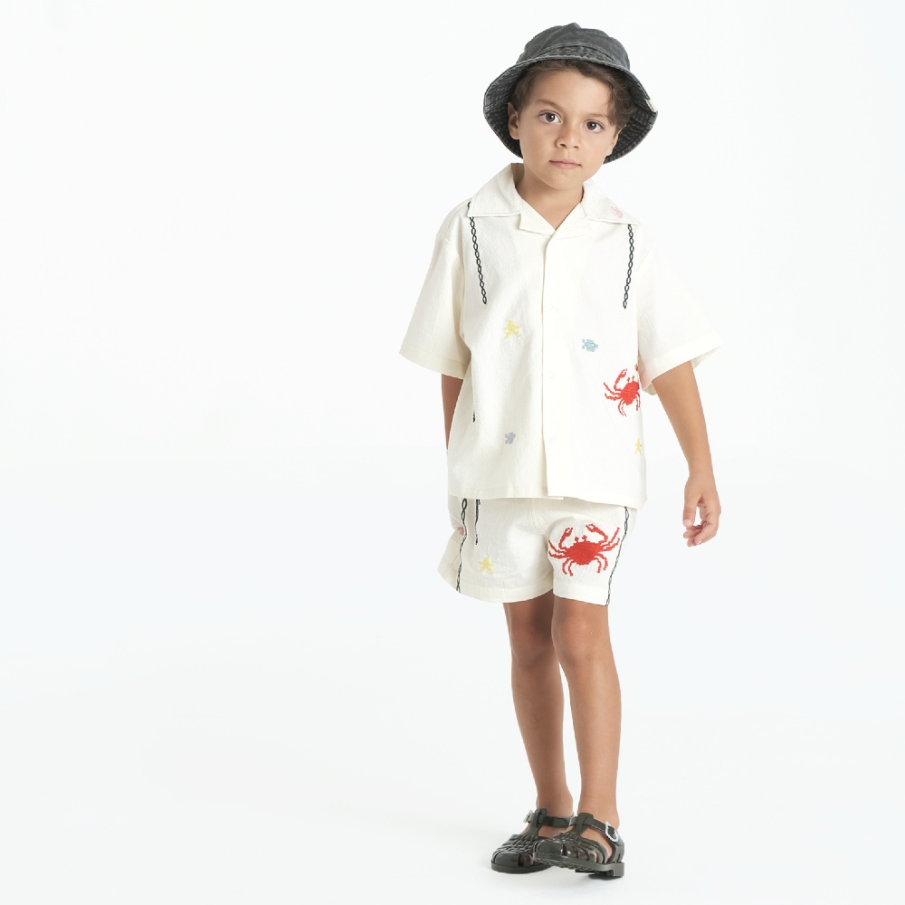 A young boy wearing a hat and white T-shirt and shorts with crab motifs on them