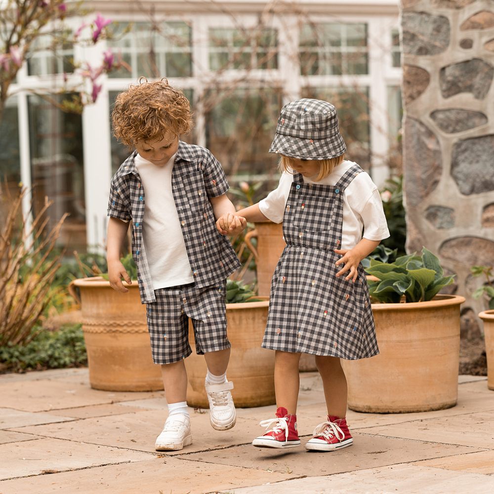 Two children wearing black and white gingham outfits stood outside holding hands 