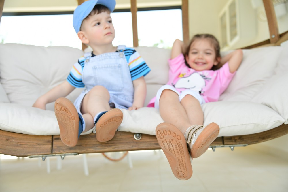 Two young children sat on a sofa with the soles of their shoes showing