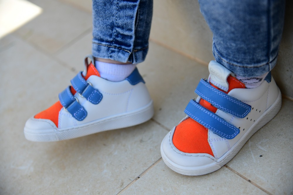A child's feet wearing white and orange trainers with blue straps by Froddo
