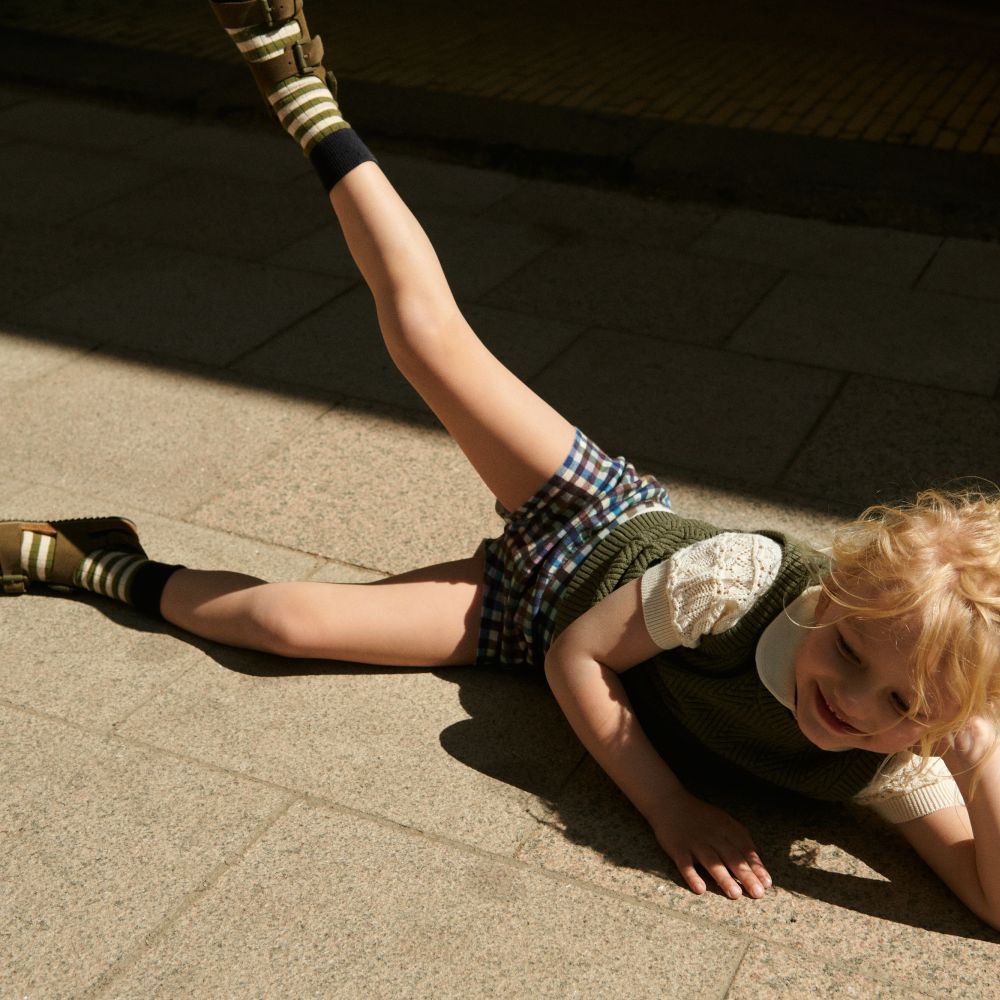 Young girl wearing shorts lying on the floor with their leg in the air 