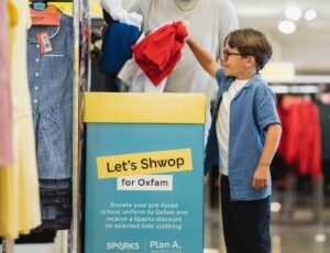 Young boy putting pre-loved school uniform in an in-store collection box