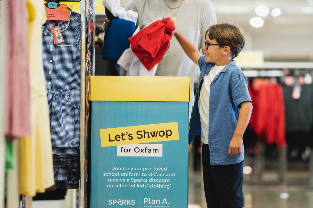 Young boy putting pre-loved school uniform in an in-store collection box
