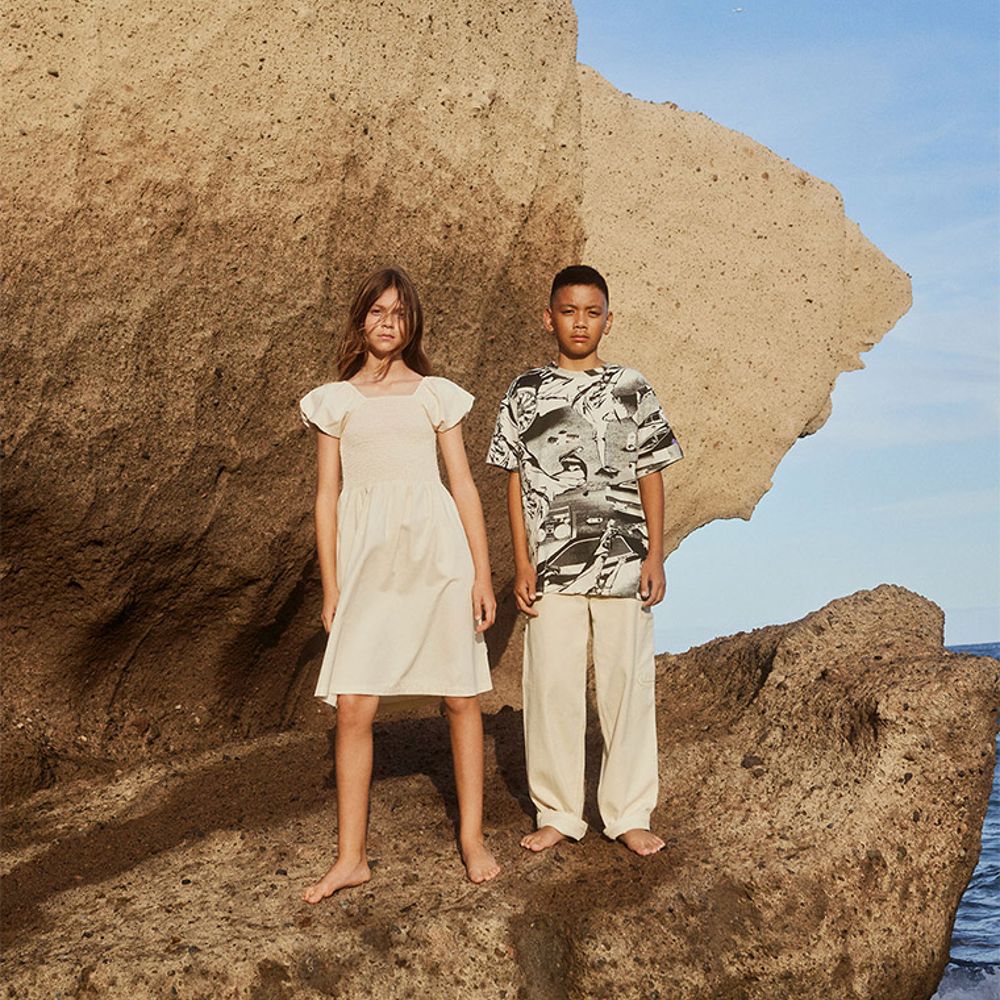 A girl wearing a white dress and a boy wearing a printed T-shirt and white trousers stood on a large rock 